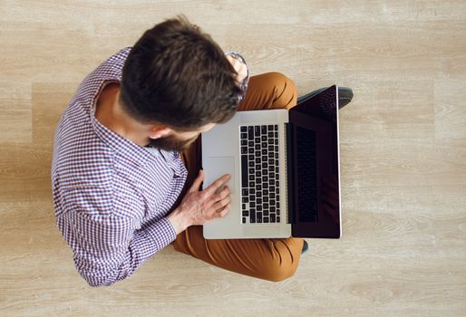 Top view of young man sitting on the floor and working with a laptop