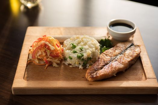 Grilled salmon with rice and vegetables at wooden table