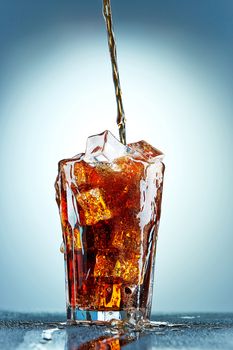 Cola pouring in a glass  with ice on a blue background