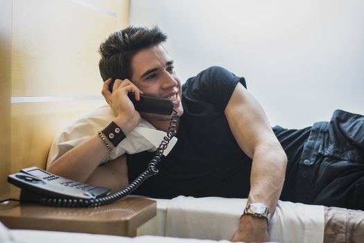 Smiling Trendy Young Man Relaxing on Bed and Talking on Telephone