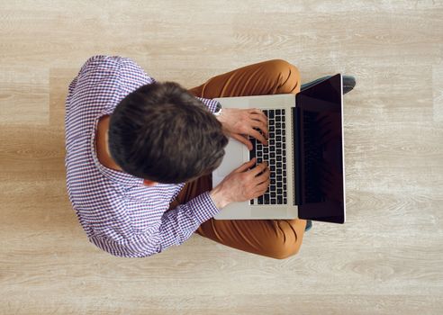 Top view of young man sitting on the floor and working with a laptop