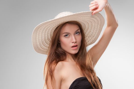 Close-up portrait of beautiful girl with hat posing in studio isolated on gray background