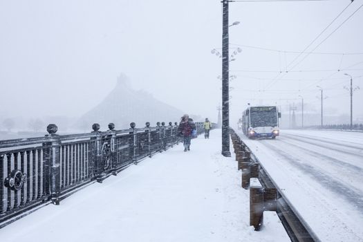 RIGA, LATVIA - DECEMBER 25, 2014: Unidentified Pedestrians and Bus with text RIGA on Stone bridge during heavy snow storm.