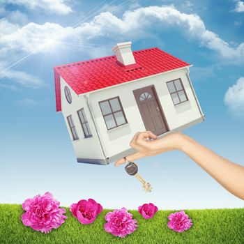 House and keys in womans hand on nature background with blue sky and pink flowers