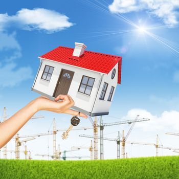 House and keys in womans hand on nature background with blue sky and building cranes