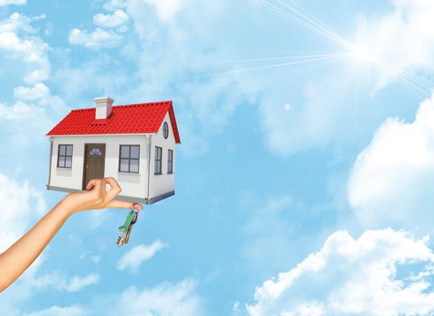 House and keys in businesswomans hand on blue sky background with bright sun