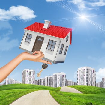 House and keys in womans hand on cityscape background with blue sky