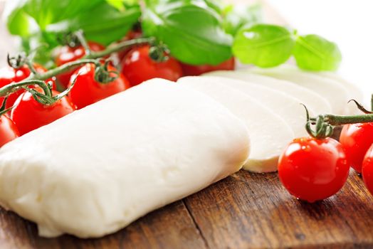 Ingredients for Caprese salad with mozzarella, tomato, basil and balsamic vinegar arranged on wooden table