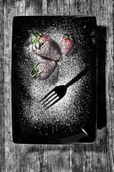 three strawberries sprinkled with sugar on a black plate and wooden base