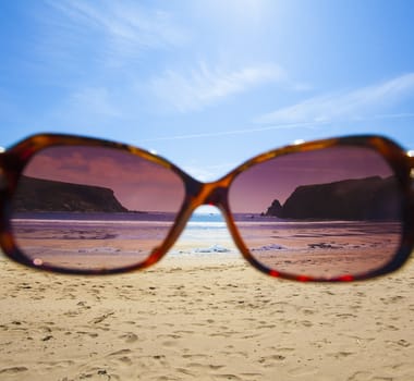 Sunglasses on a colourful beach towel on a sandy beach