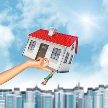 House in businesswomans hand with cityscape on blue sky background 