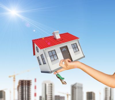 House in businesswomans left hand with cityscape on blue sky background 