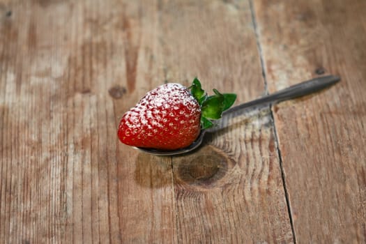 small strawberry on a teaspoon and wooden base