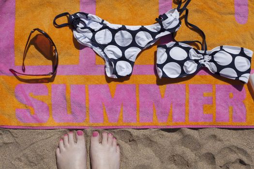 Feet view of colourful beach towel, bikini and sunglasses