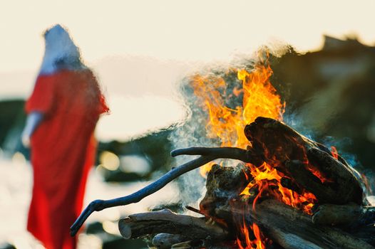 Woman in red dress near the campfire on the coast