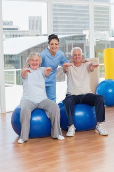 Portrait of senior couple on exercis ball with trainer in gym