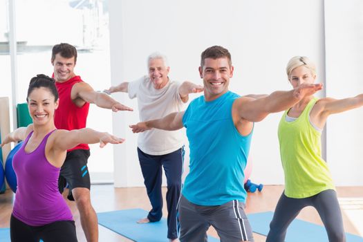 Happy men and women doing warrior pose in yoga class