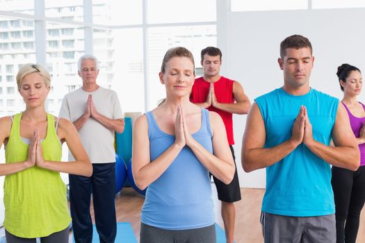 Fit men and women meditating with hands joined in fitness club