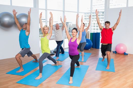 Full length of people with hands raised doing yoga at fitness club