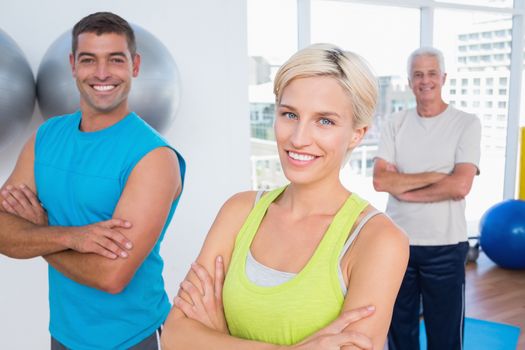 Portrait of happy woman with male friends standing arms crossed at gym class