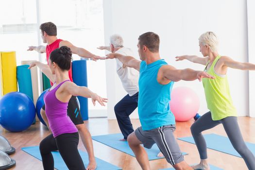 Fit men and women doing warrior pose in yoga class