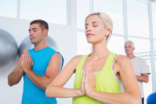 Fit people meditating with hands joined in gym class