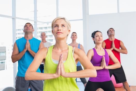 Female instructor with class meditating in fitness club