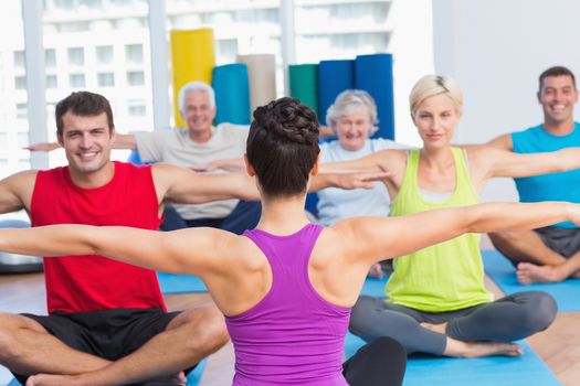 Female instructor with class practicing yoga in health club