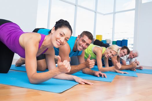 Portrait of happy people gesturing thumbs up while lying on exercise mats at gym