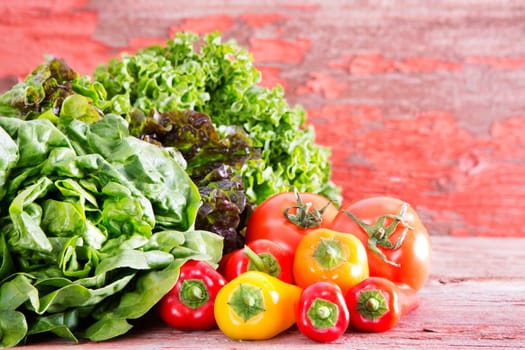 Healthy fresh salad ingredients at a farm market with assorted lettuce varieties displayed on rustic wooden boards with ripe red tomatoes and sweet bell peppers, with copyspace