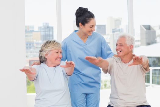 Happy female trainer assisting senior couple to exercise in gym