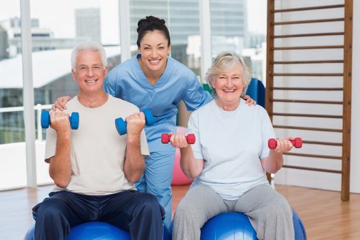 Portrait of happy female instructor with arms around senior couple in gym