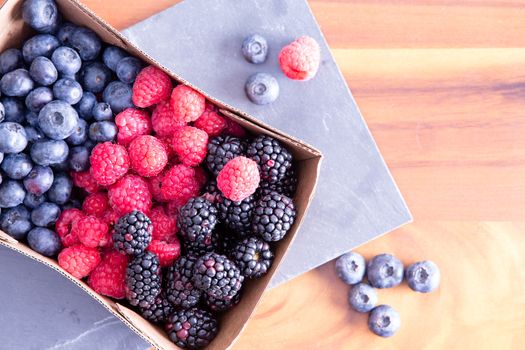 Box of fresh seasonal autumn berries with blueberries, blackberries, and raspberries displayed in a punnet on a wooden table fresh from the farmers market, with copy space