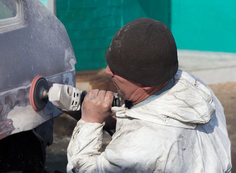 Worker performs repairing car body leveling putty before painting