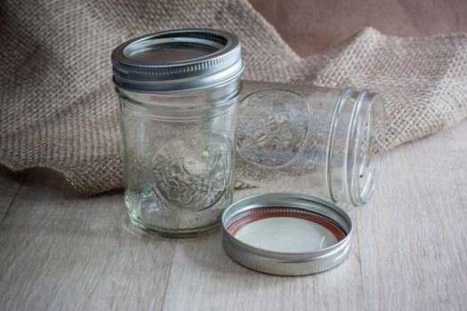 glass canning jars on a wooden table with burlap behing them.