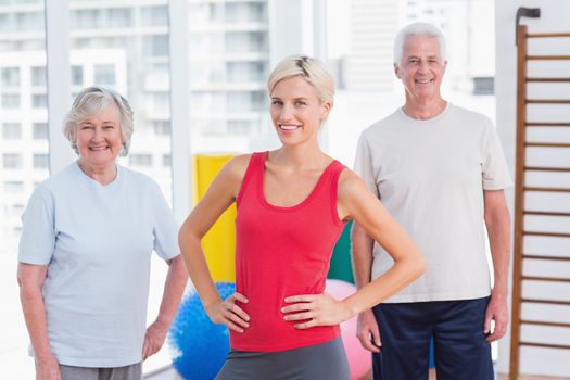 Portrait of confident female instructor with senior couple in gym