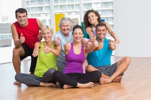 Full length portrait of fit men and women gesturing thumbs up in fitness studio