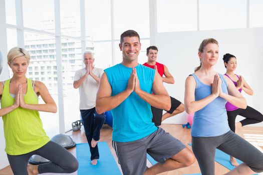 Happy men and women practicing tree pose in fitness studio