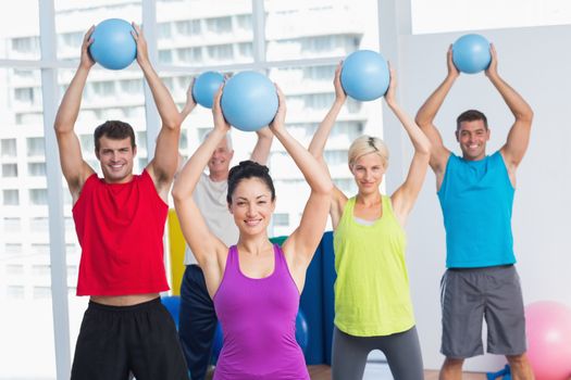 Portrait of female instructor with class exercising with fitness balls in health club