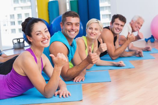 Portrait of happy people gesturing thumbs up while lying on exercise mats at gym