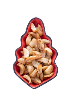 Roasted spicy marinated garlic cloves in a decorative leaf-shaped glazed pottery dish viewed from overhead centered on a white background