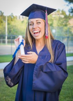 Excited and Expressive Young Woman Holding Diploma in Cap and Gown Outdoors.