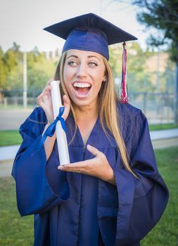 Excited and Expressive Young Woman Holding Diploma in Cap and Gown Outdoors.