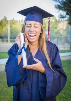 Excited and Expressive Young Woman Holding Diploma in Cap and Gown Outdoors.