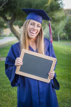 Excited Young Woman Holding Diploma and Blank Chalkboard Wearing Cap and Gown Outdoors.