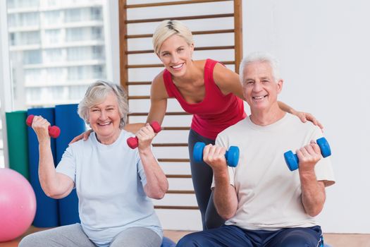 Portrait of happy female trainer with senior couple in fitness studio