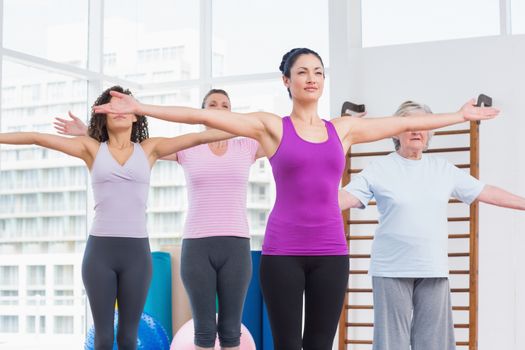 Female friends with arms outstretched exercising in gym