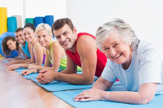 Portrait of happy senior woman with friends lying on exercise mats at gym