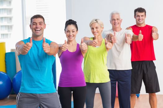 Portrait of cheerful men and women gesturing thumbs up at gym