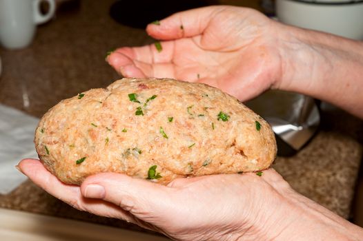 Cook prepares meatloaf holds in one hand and a second hand corrects the shape roll
